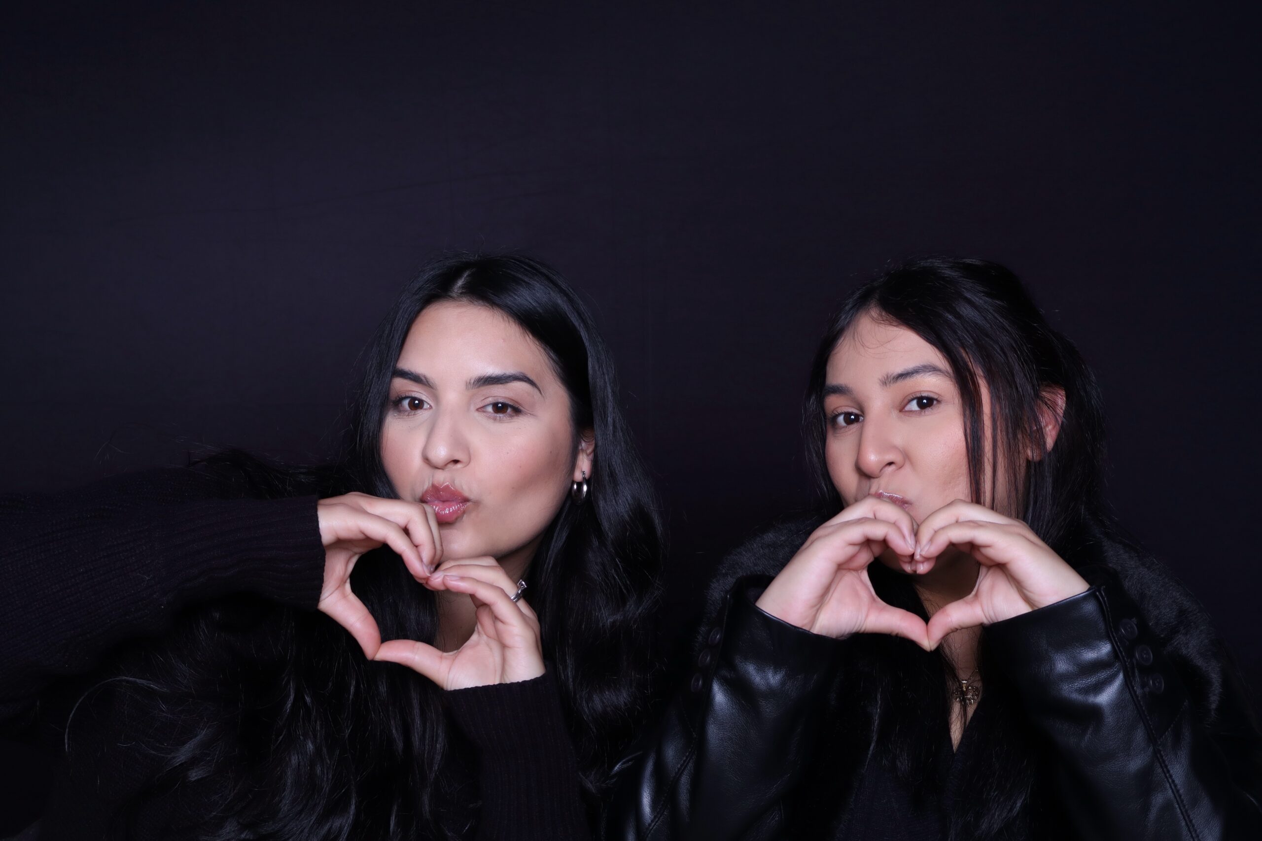 Two guests posing with heart hand gestures at a modern photo booth with studio lighting