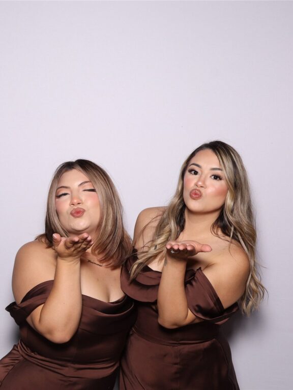 Two guests posing together against a light photo booth backdrop